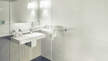 A modern bathroom with a white sink, mirror, and glass shower enclosure.
