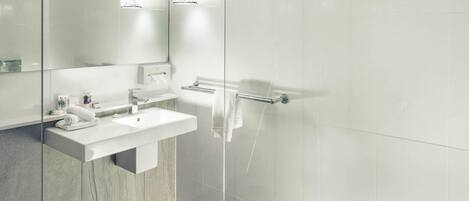 Un baño moderno con lavamanos blanco, espejo y cabina de ducha con vidrio.