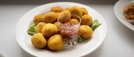 Un piatto di crocchette dorate con un bicchiere di salsa rossa e una guarnizione di foglie verdi.