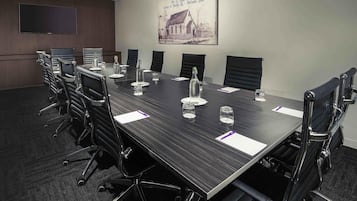 A conference room with a long table, black chairs, water bottles, and a mounted television.