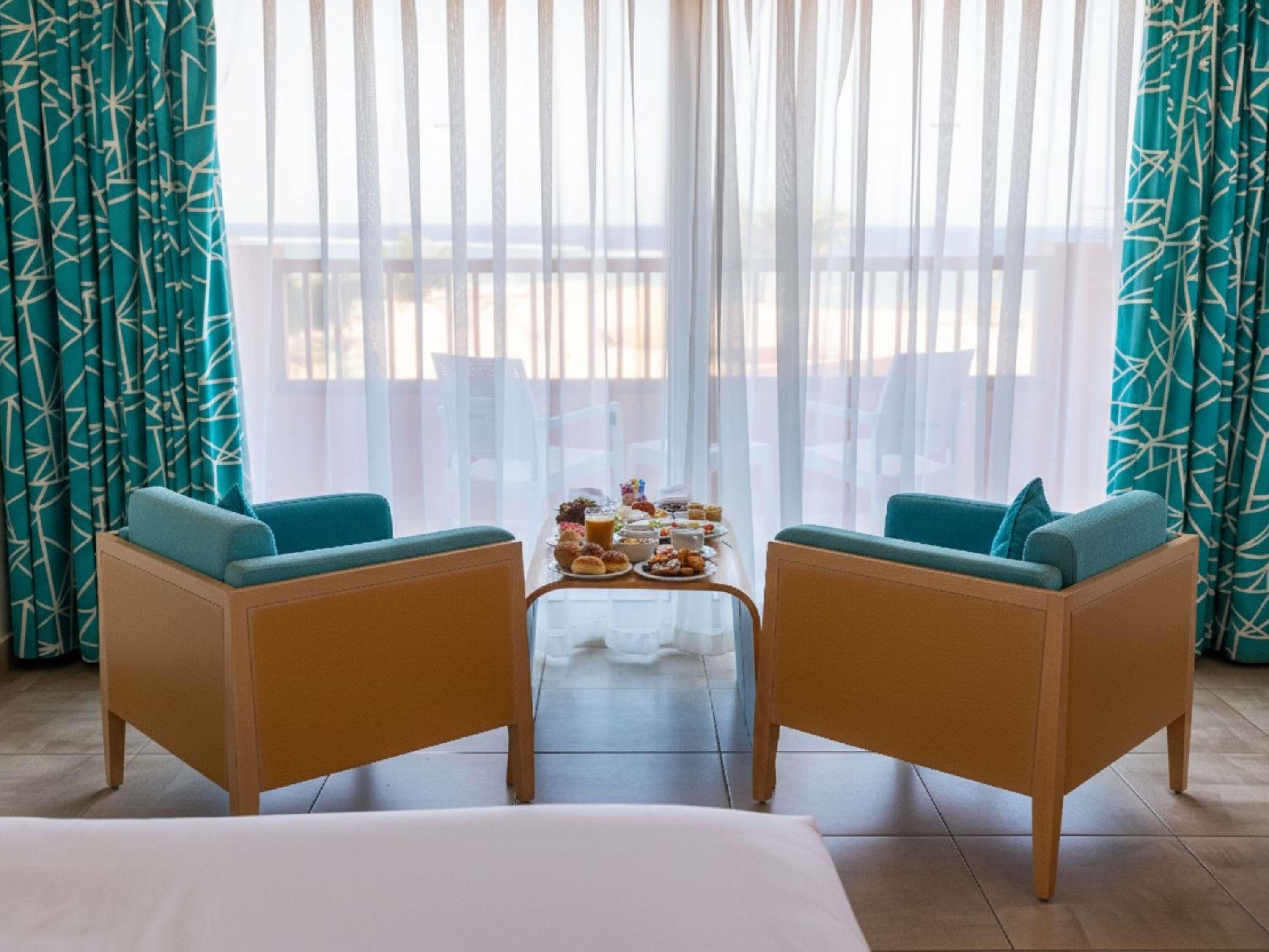 Una habitación con dos sofás, una pequeña mesa con comida y vistas al balcón.