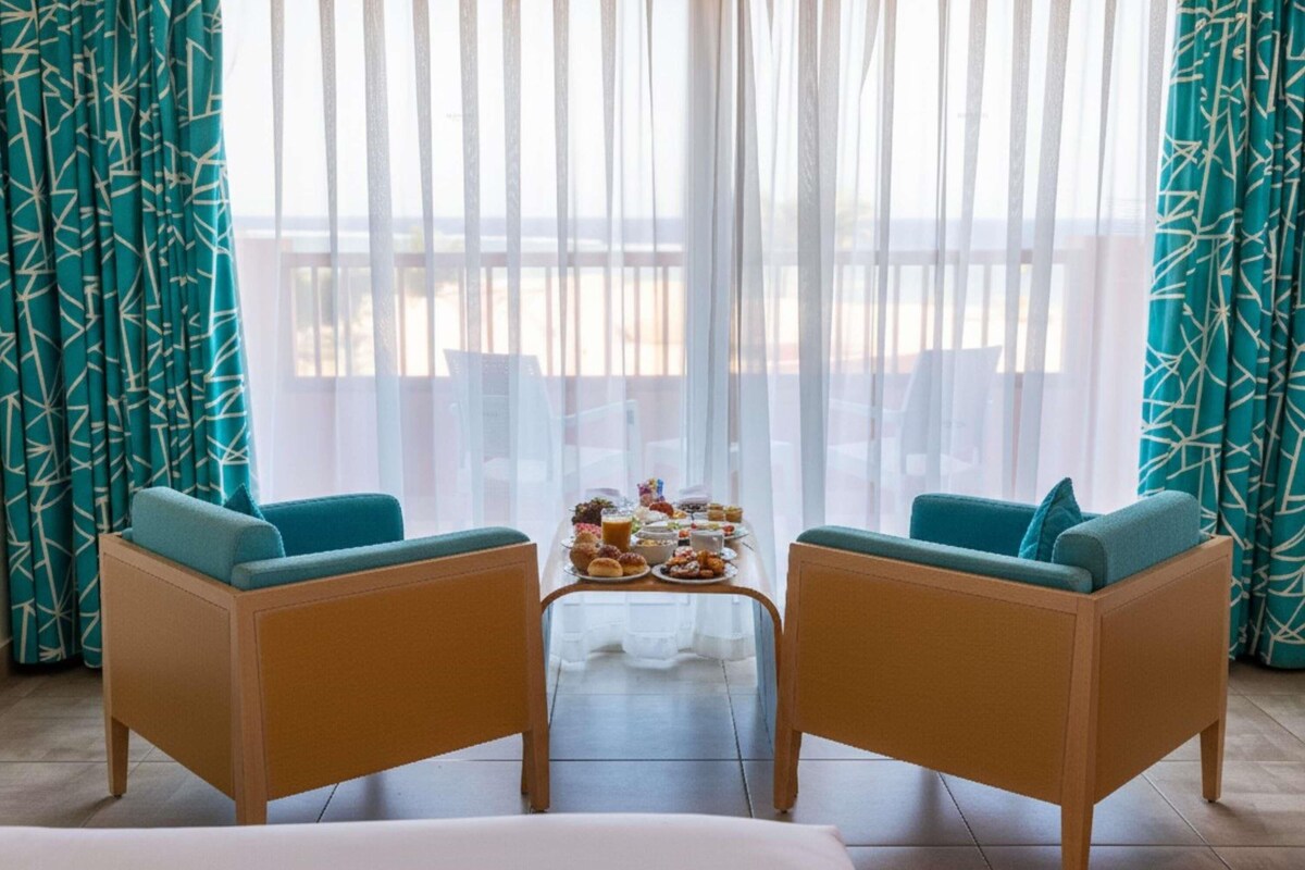 A room with two sofas, a small table with food, and a balcony view.