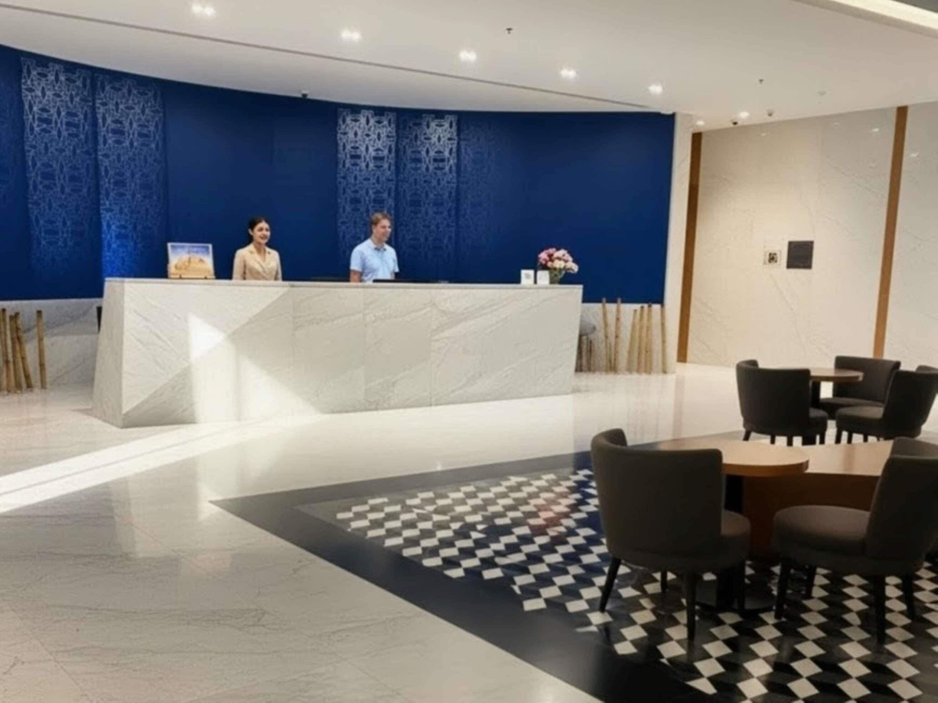 A reception area with a marble counter, two staff members, a checkered floor, and a seating area with chairs.