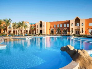A hotel with a large swimming pool, palm trees, and a modern building with arched windows. - Novotel Marsa Alam Beach Resort (El Quseir)