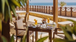 A dining area with wicker furniture, a table set with plates, cups, and a fruit basket. - Novotel Marsa Alam Beach Resort (El Quseir)