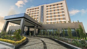 Ein modernes Hotel mit einem gut sichtbaren 'NOVOTEL'-Schild, einem zentralen Eingangsbereich und einem angelegten Garten.