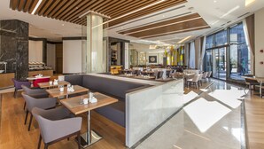 Ein modernes Restaurant mit hohen Decken, Holzvertäfelung und verschiedenen Sitzgelegenheiten, darunter Sitzecken und Tische.