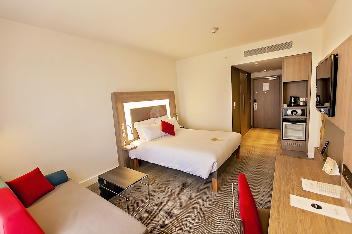 Een hotelkamer met een bed, een klein bureau, een stoel, een televisie en een kitchenette.