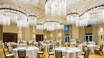 A banquet hall with round tables set for dining, large chandeliers, and a carpeted floor.