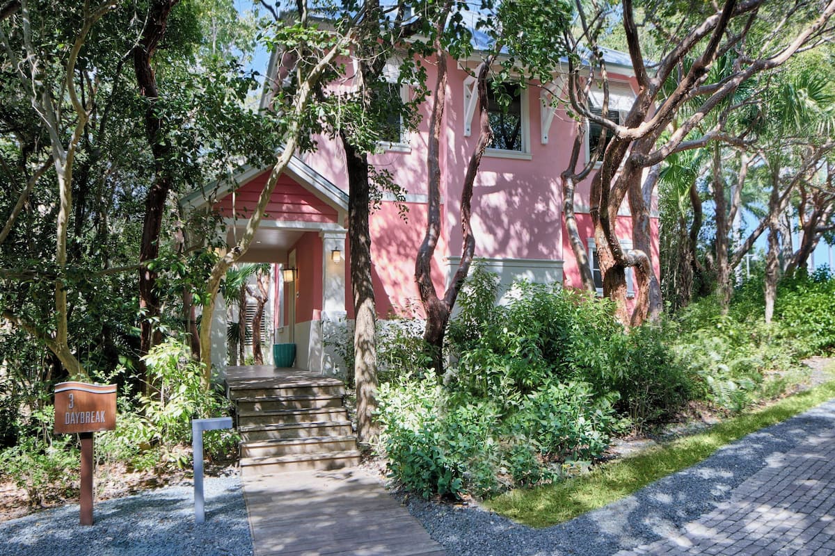 A pink house with a front porch, surrounded by trees and greenery.