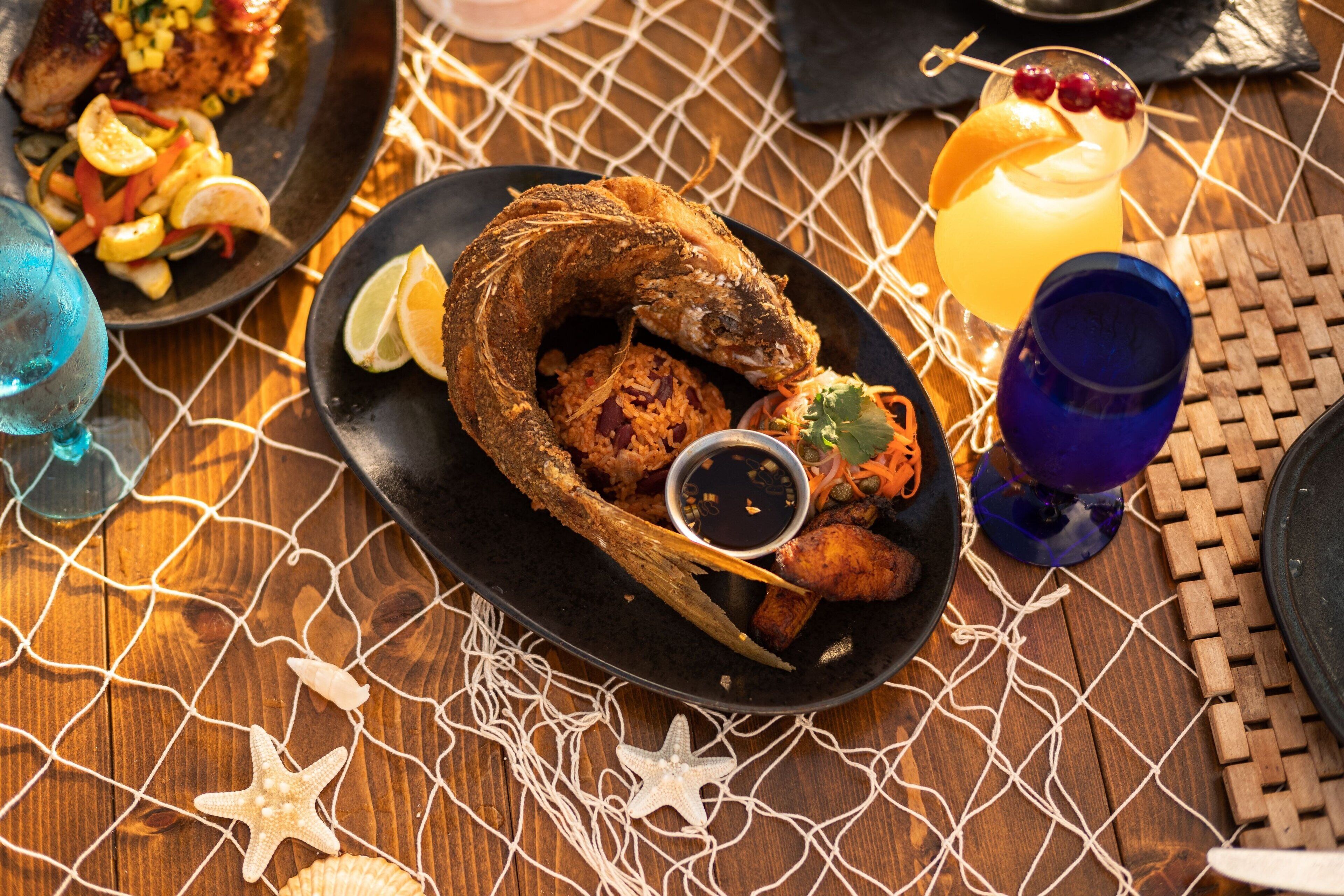 A seafood dish with a lemon wedge, a drink with a garnish, and a starfish decoration on a wooden table.
