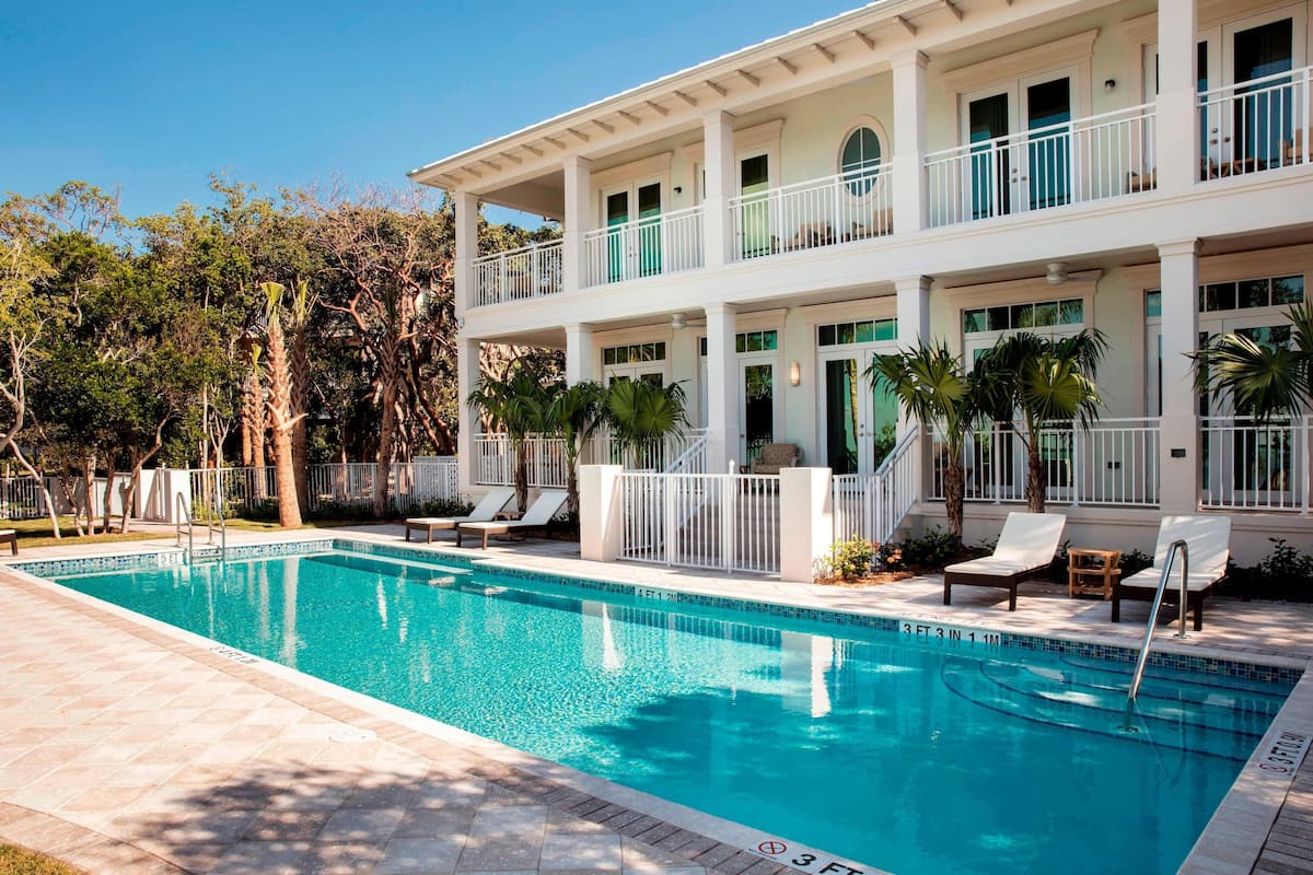 A two-story building with a swimming pool, outdoor seating, and a tropical garden.