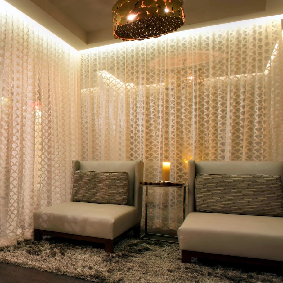 A modern room with two sofas, a small table, and a decorative lamp. A wooden door leads to another room, and the walls have a patterned wallpaper.