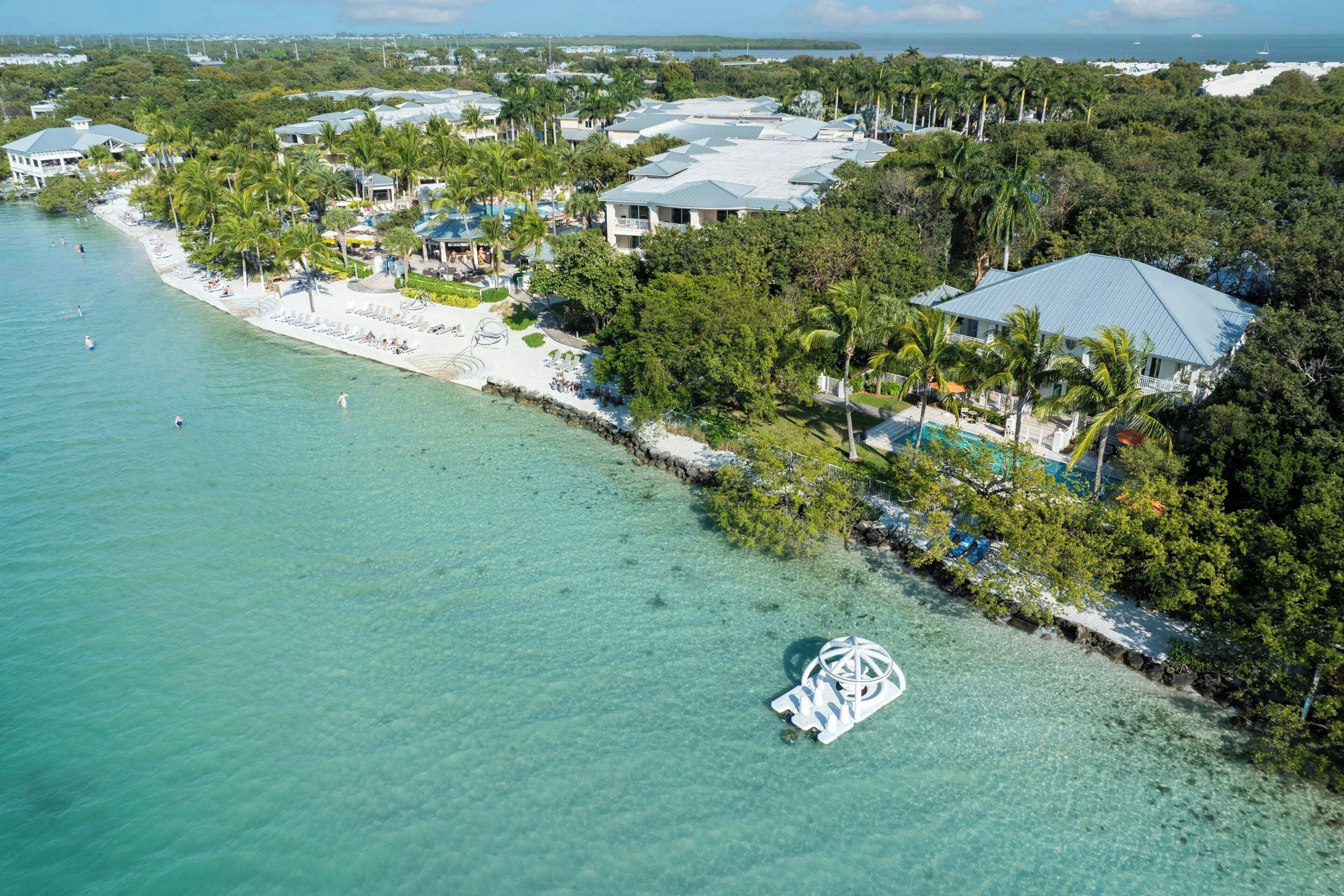 Eine Luftaufnahme eines Küstenresorts mit Strand, klarem türkisblauem Wasser und üppiger Vegetation.