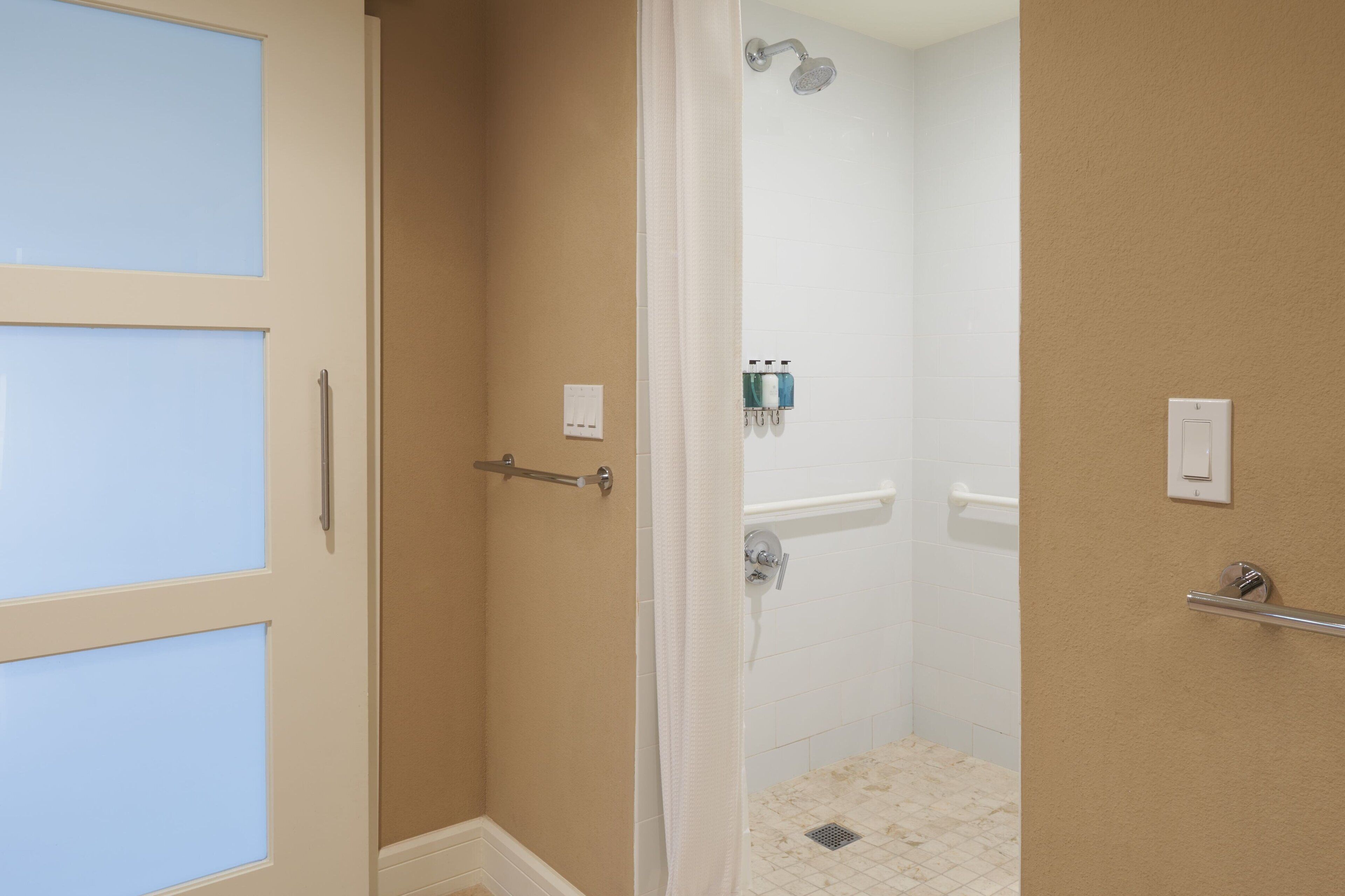 Uma casa de banho com chuveiro, porta-toalhas e suporte para papel higiénico.
