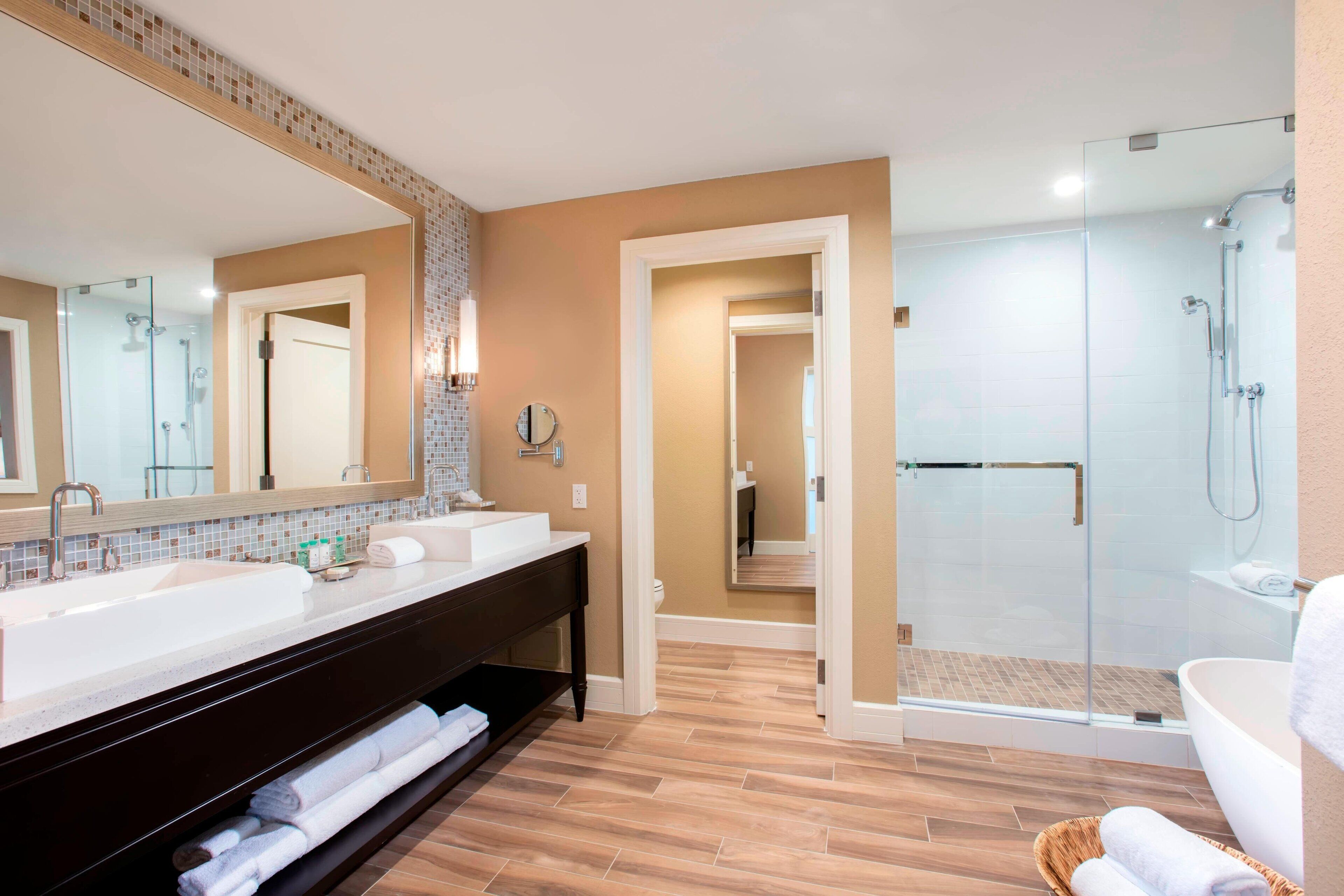 A modern bathroom with two sinks, a large mirror, a walk-in shower, and a bathtub.