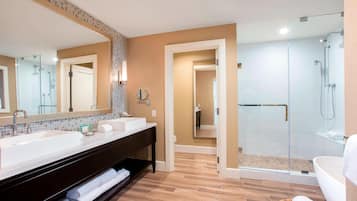 A modern bathroom with two sinks, a large mirror, a walk-in shower, and a bathtub.