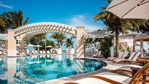 Un espace piscine avec des chaises longues et des parasols, un ciel dégagé et des palmiers.