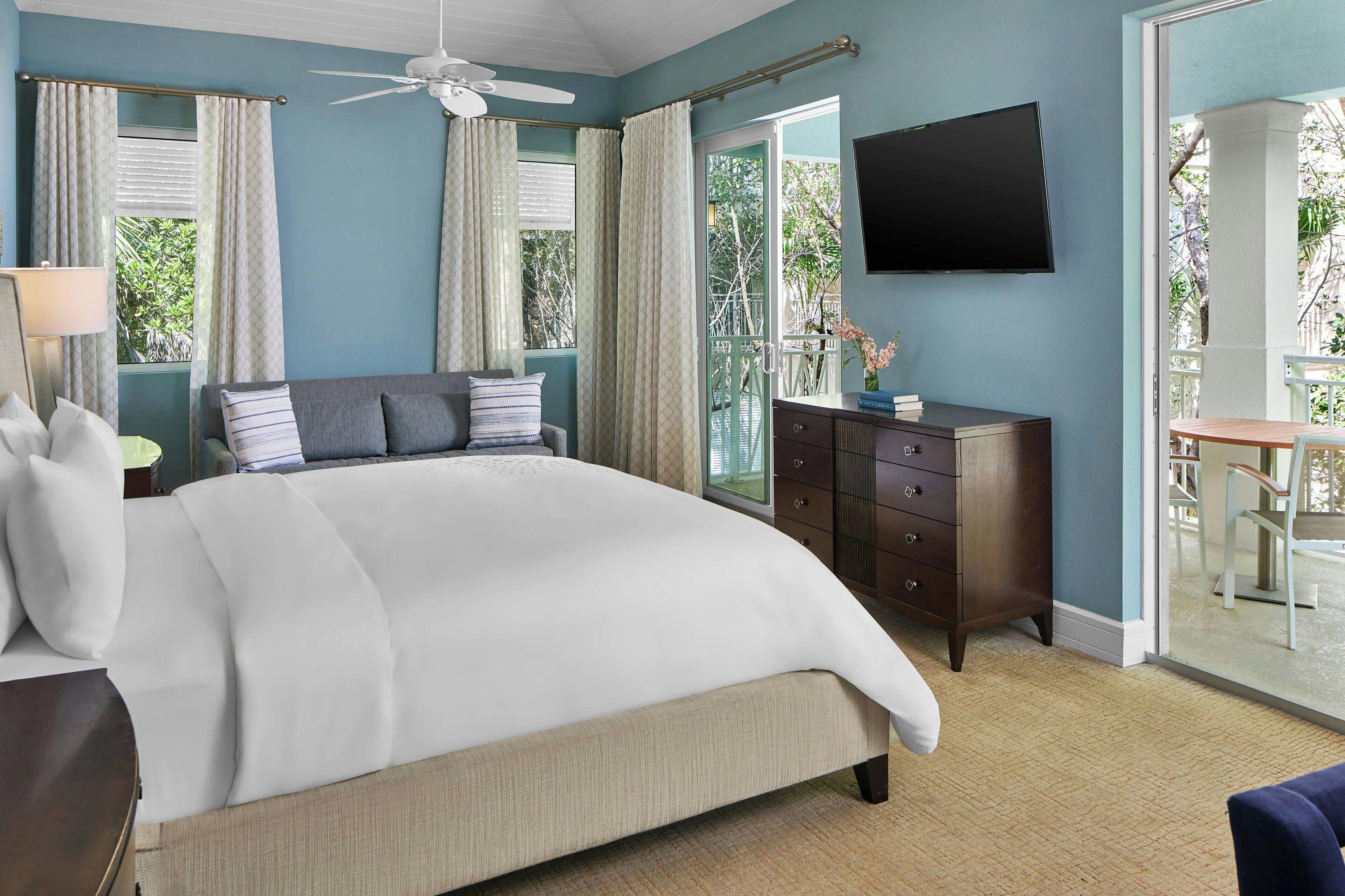 A bedroom with a bed, a dresser, a TV, and a balcony with a table and chairs.