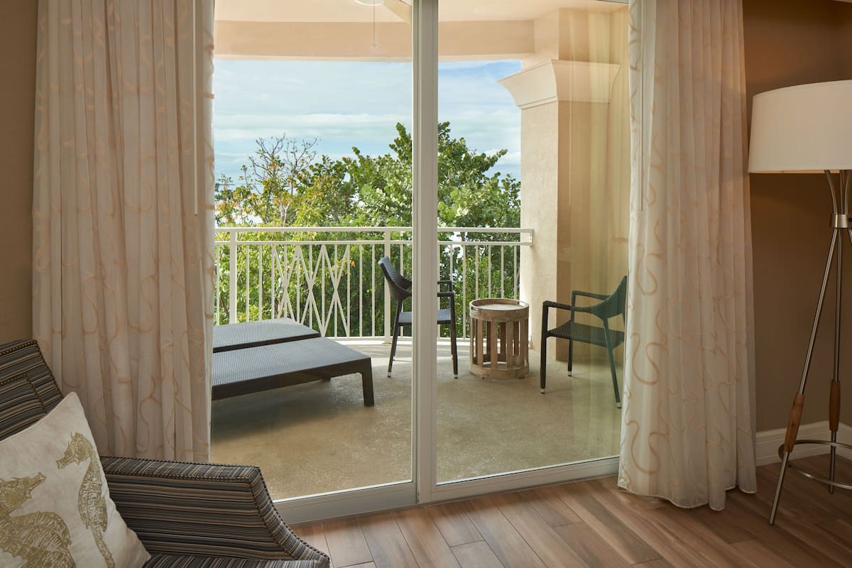 A room with a sliding glass door leading to an outdoor balcony with a table, chairs, and a sofa.