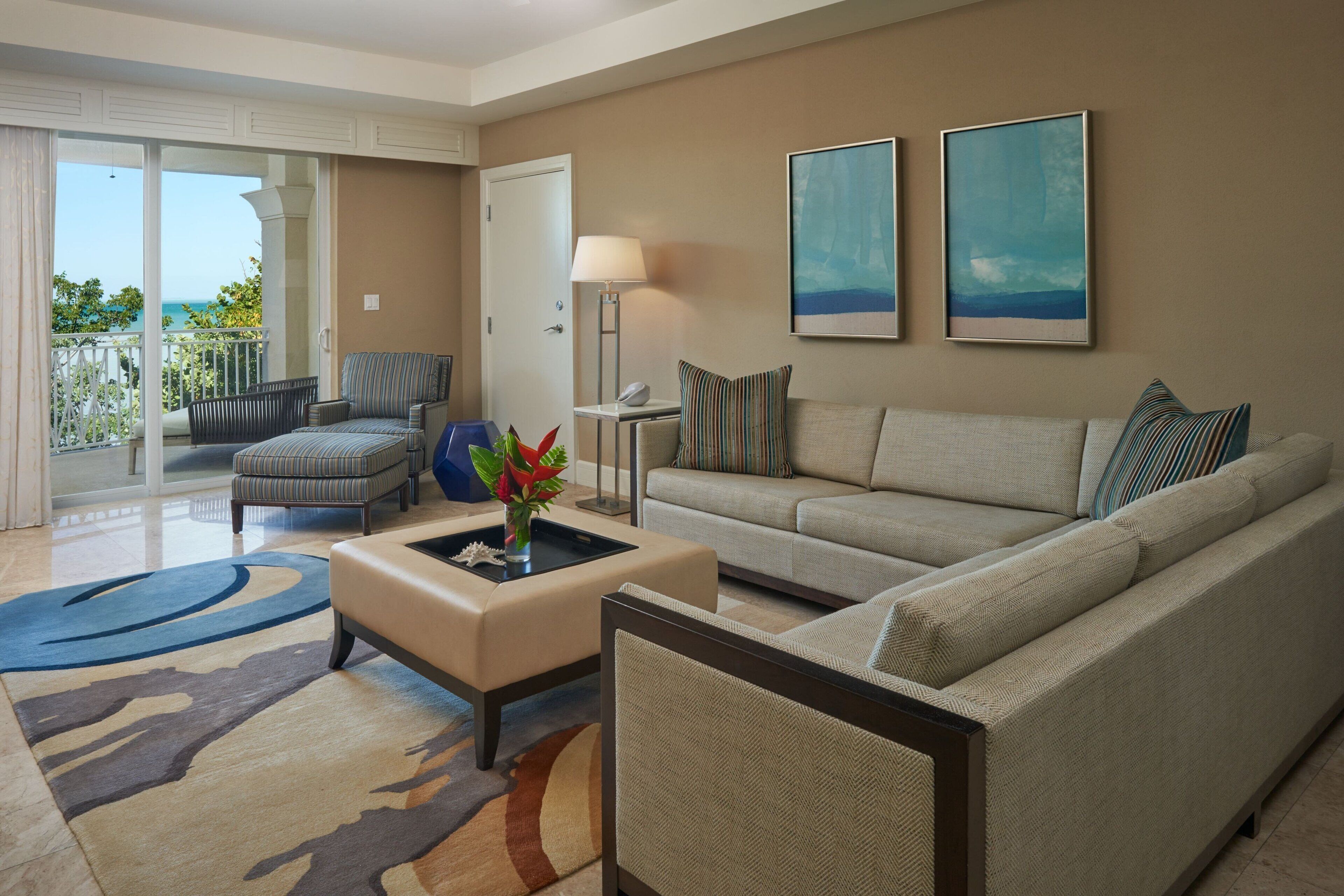 A living room with a sofa, armchair, and ottoman, a vase with flowers, and two framed artworks on the wall.