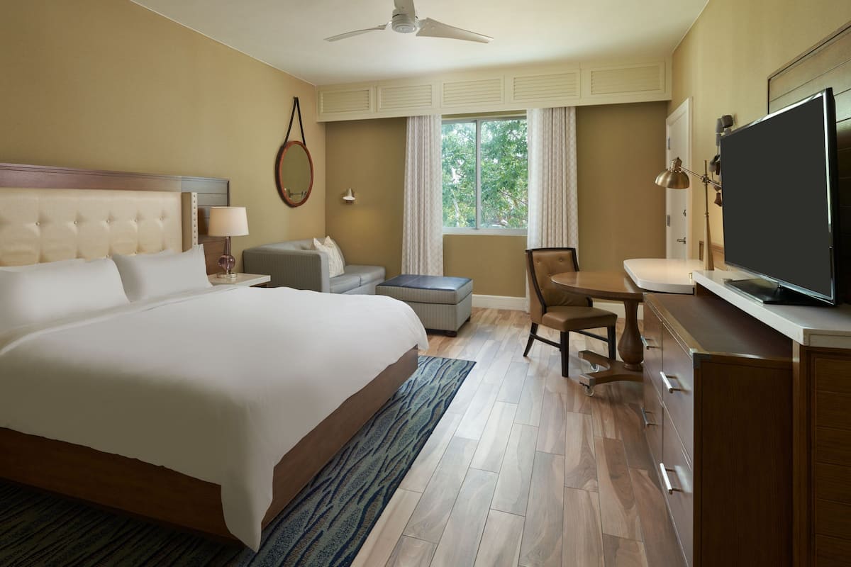 A hotel room with a large bed, a desk with a chair, a television, and a window with curtains.