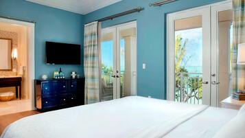 A bedroom with a large bed, a dresser, a television, and a balcony with a view of the ocean.