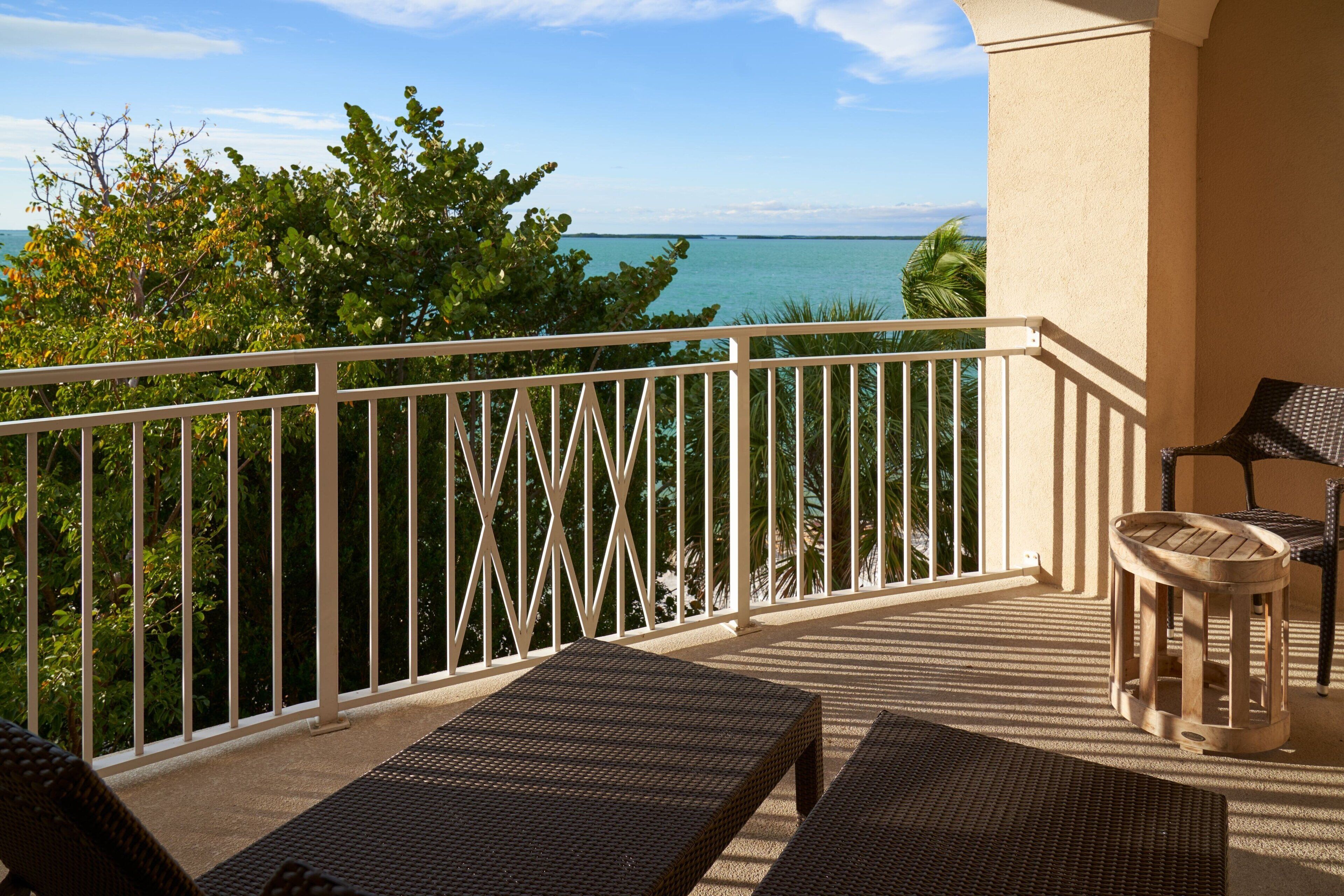 Een balkon met twee rieten lounge fauteuils, een bijzettafeltje en uitzicht op de oceaan.