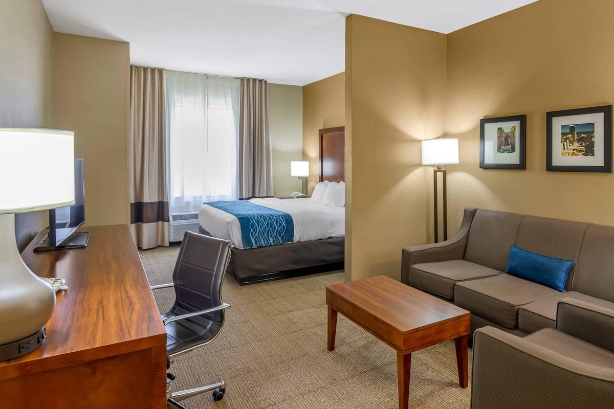 Une chambre d’hôtel comprenant un lit, un bureau avec une lampe, un canapé, une chaise et une petite table.