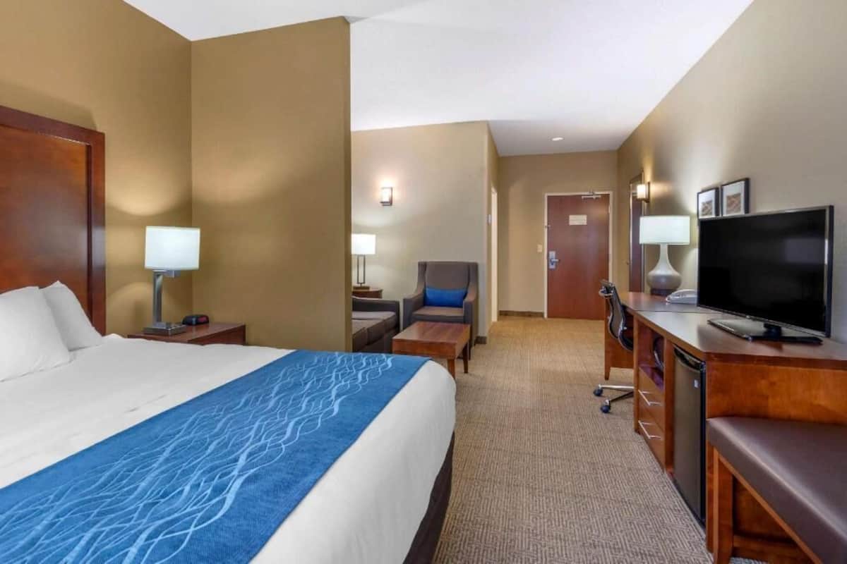 Une chambre d’hôtel avec un grand lit, un bureau avec une télévision, une chaise et une lampe.