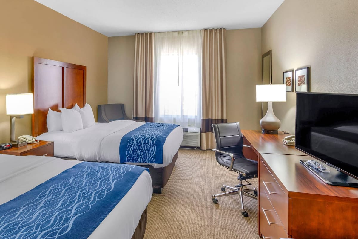 Une chambre d’hôtel avec deux lits, un bureau avec une télévision, une chaise et une lampe.