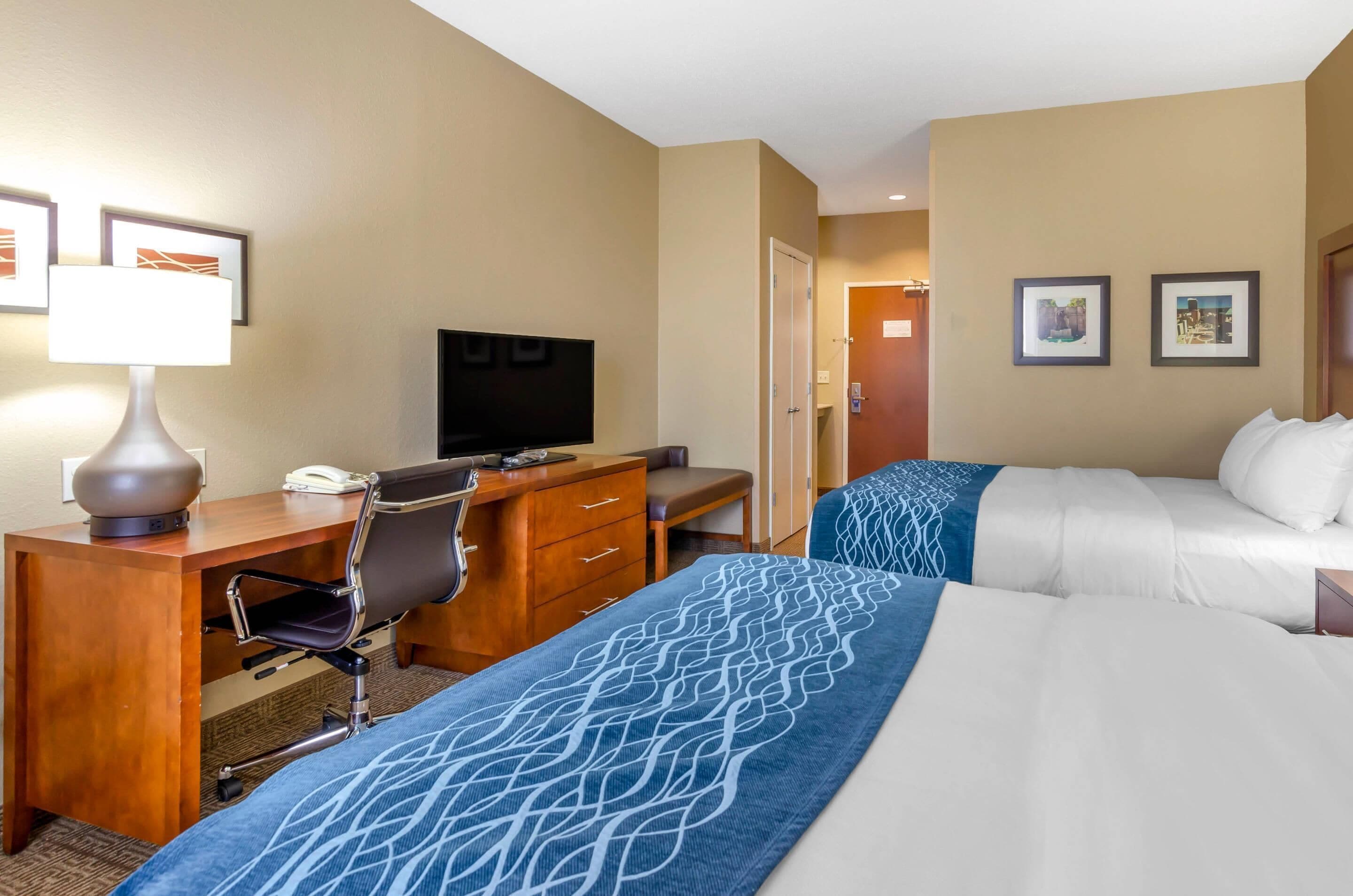 A hotel room with a desk, chair, television, two beds, and a door.