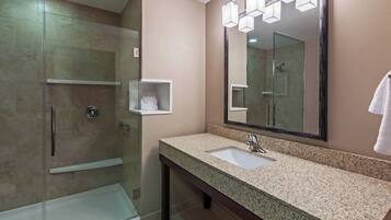 A modern bathroom with a glass-enclosed shower, a sink with a large mirror, and a towel rack.