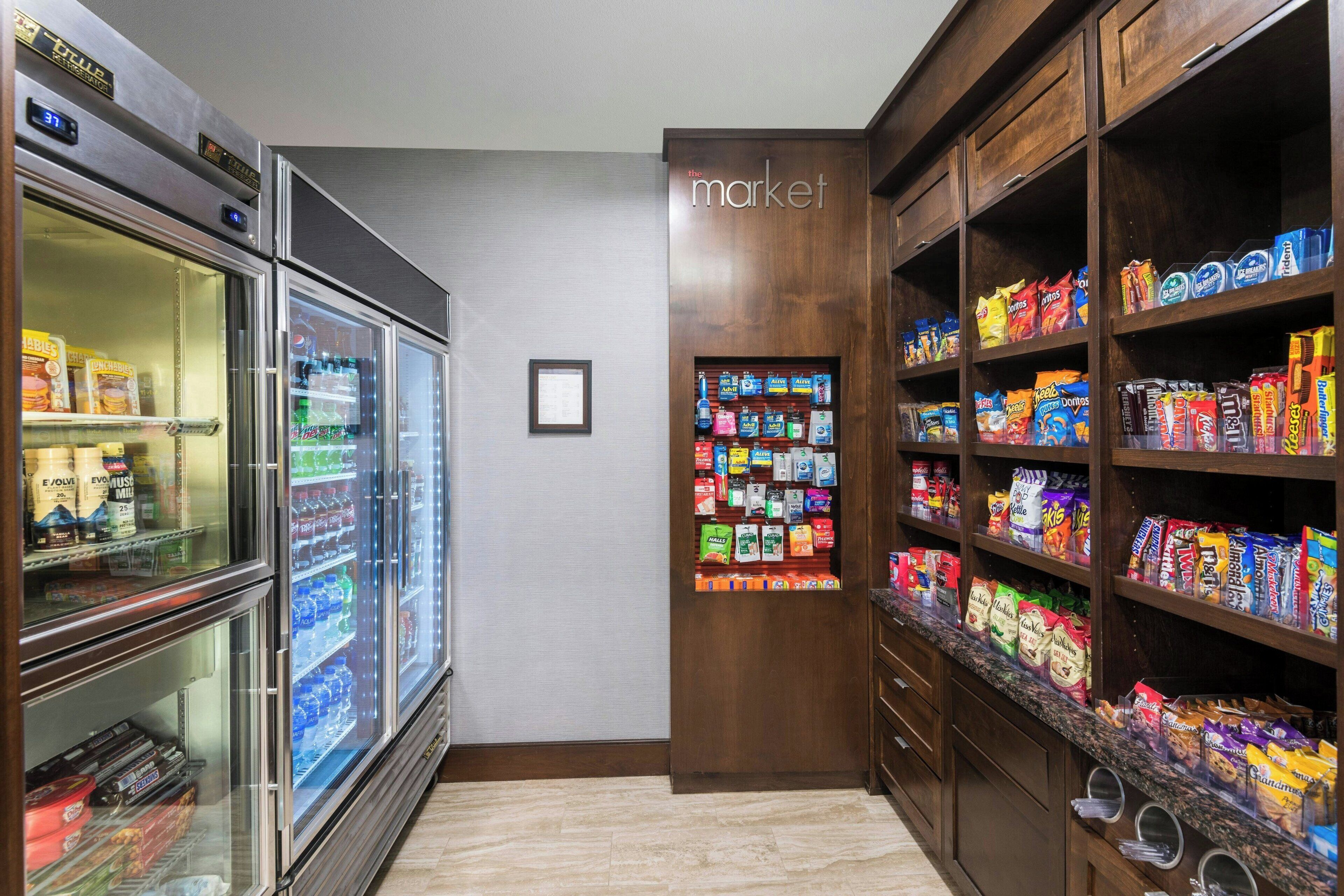A hotel room with a minibar, a refrigerator stocked with beverages, and shelves with snacks and toiletries.