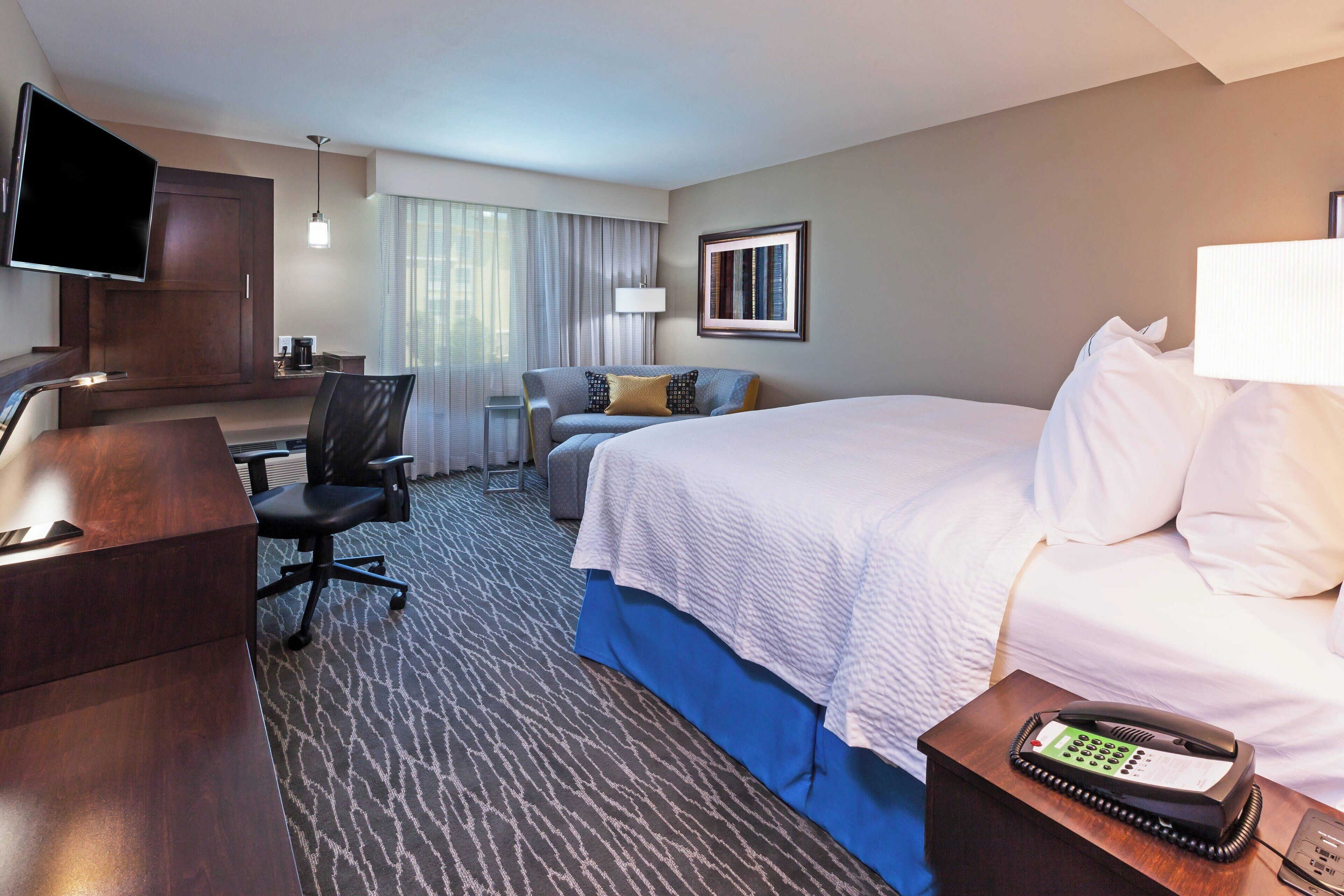 A hotel room with a bed, a desk with a chair, a television, a telephone, and a window with curtains.