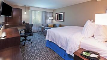 A hotel room with a bed, a desk with a chair, a television, a telephone, and a window with curtains.