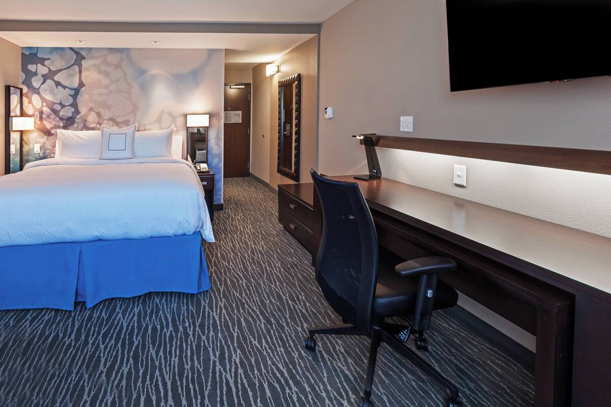 Habitación de hotel con una cama grande, un escritorio con silla, un televisor de pantalla plana y un espejo.