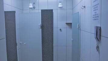 A restroom with three stalls, each with a door and a towel rack. There is a wall-mounted telephone and a sign with instructions.