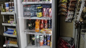 A refrigerated display case stocked with various beverages and snacks, including cans, bottles, and packaged goods, with price tags visible.