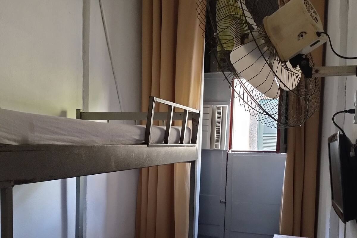 Habitación con literas, un escritorio, una silla, un ventilador y un televisor.
