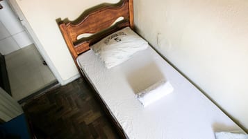 Een kleine kamer met een enkel bed, een houten hoofdbord, een wit matras en een kussen met tekst.