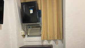A hotel room with a bed, a heater, a TV, and a window with curtains.
