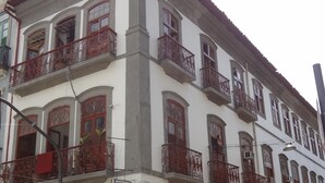 A building with a white facade, multiple balconies with red railings, and storefronts with signs advertising food items.
