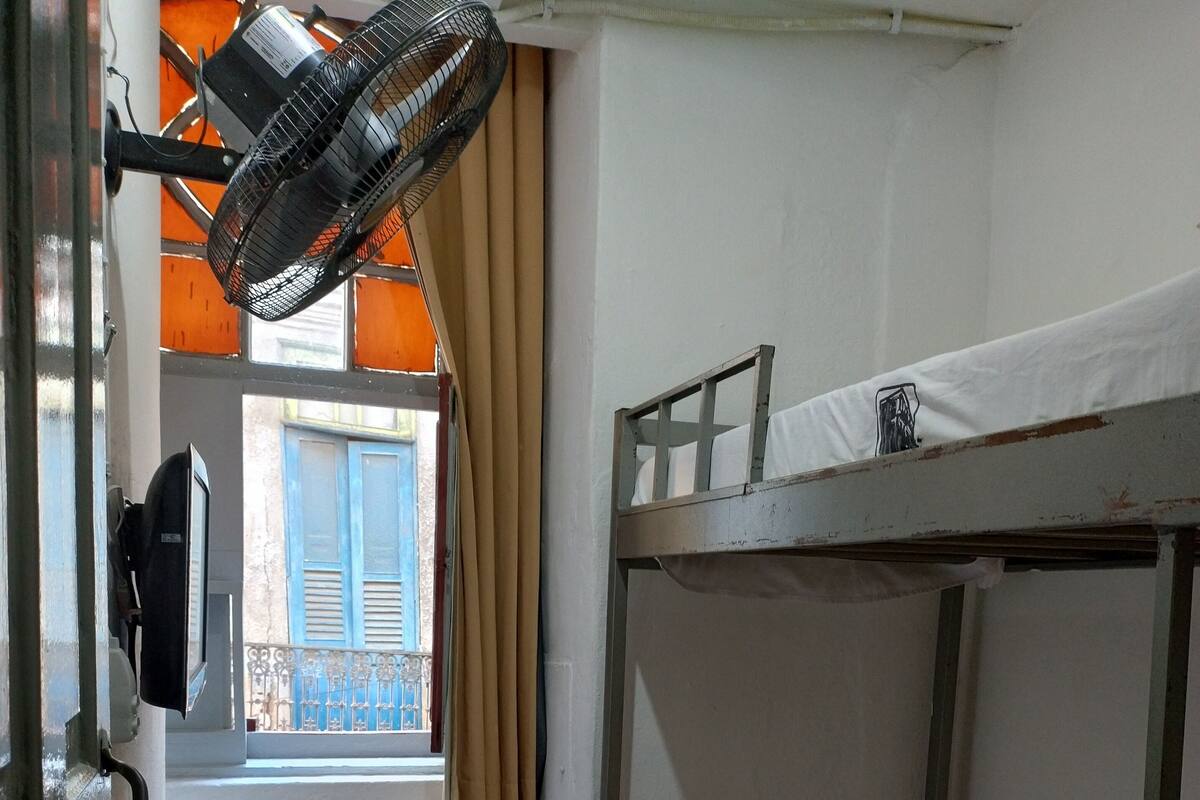 Habitación con literas, un escritorio, un ventilador, una ventana con cortinas y vistas al balcón exterior.