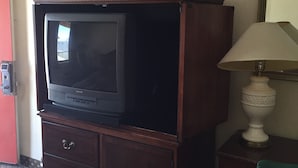 Ein Hotelzimmer mit einem Holz-Fernsehschrank, einem Fernseher, einer Lampe und einem Bett mit einem gemusterten Überwurf.