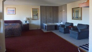 Ein Hotelzimmer mit Bett, Schreibtisch, Sessel, Sofa, Badezimmer und Spiegel.
