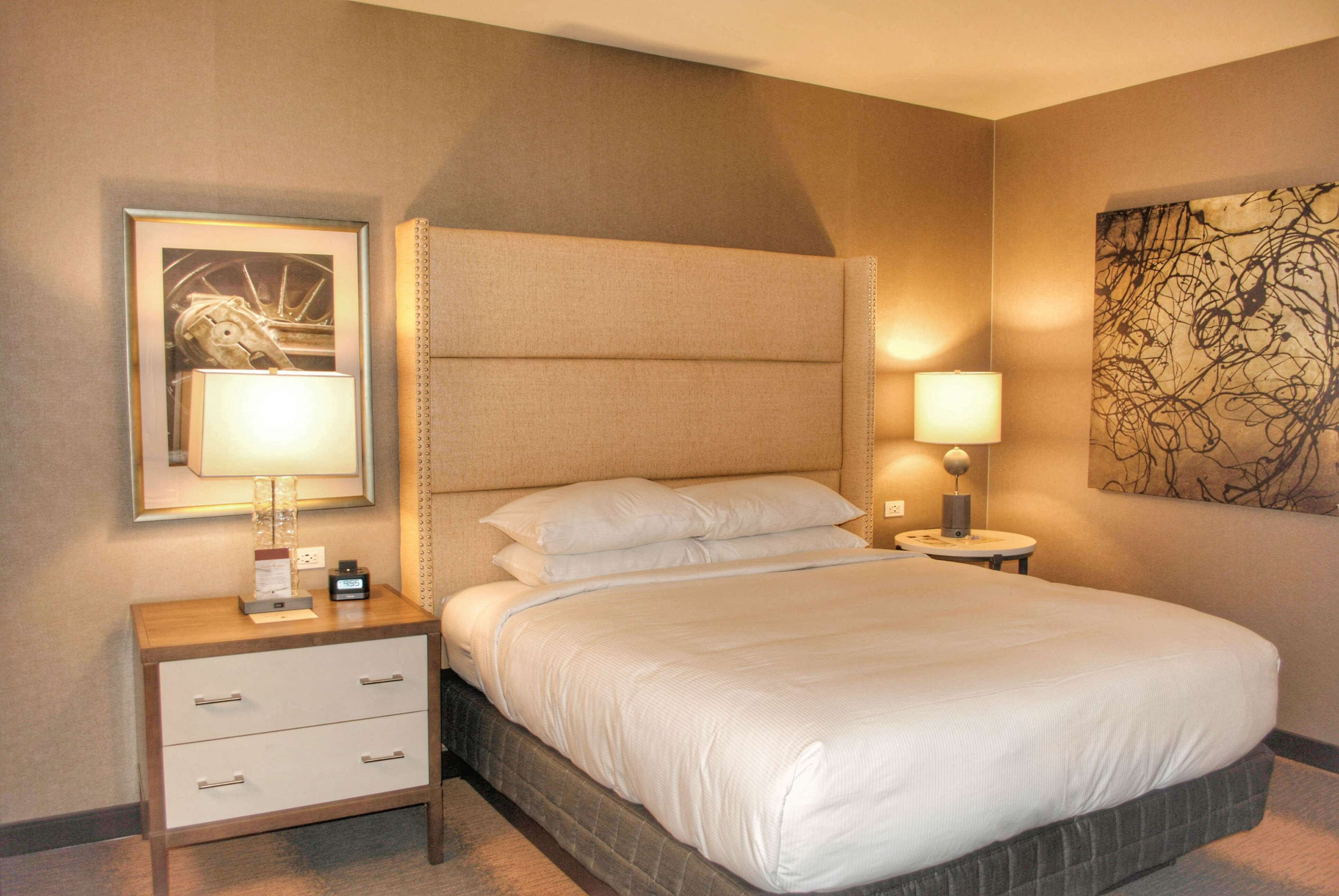 A hotel room with a large bed, a nightstand with drawers, a framed picture, and a wall art piece.