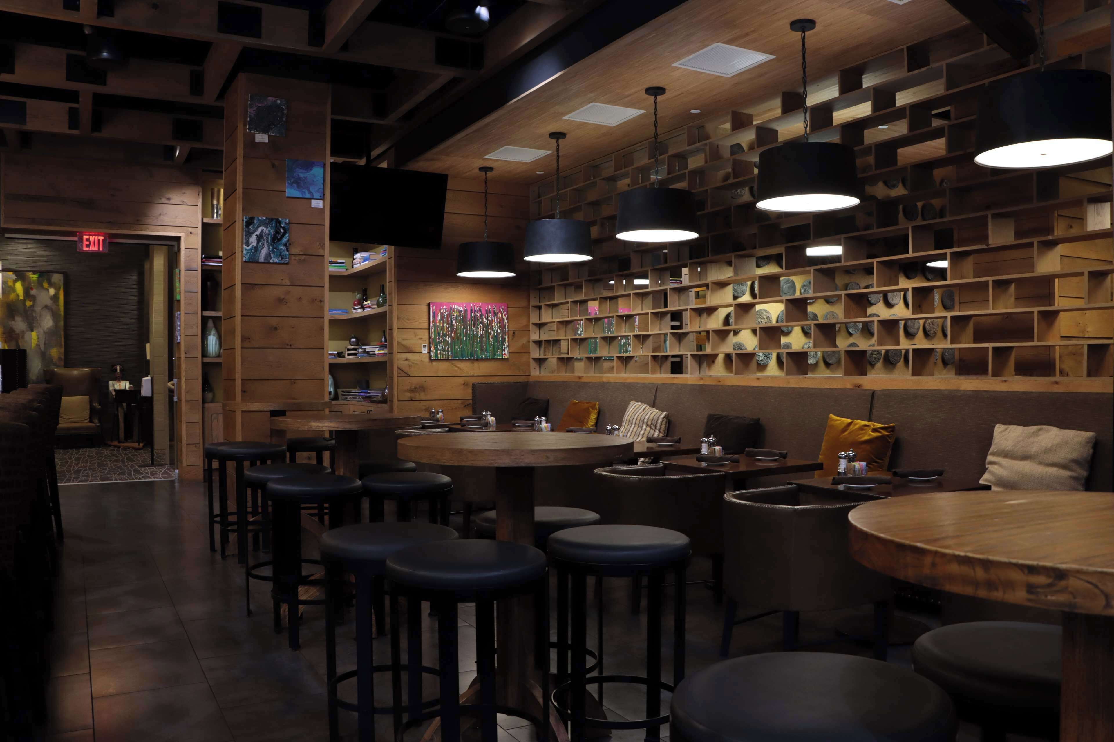 A cozy bar area with wooden shelves, hanging lights, and stools.