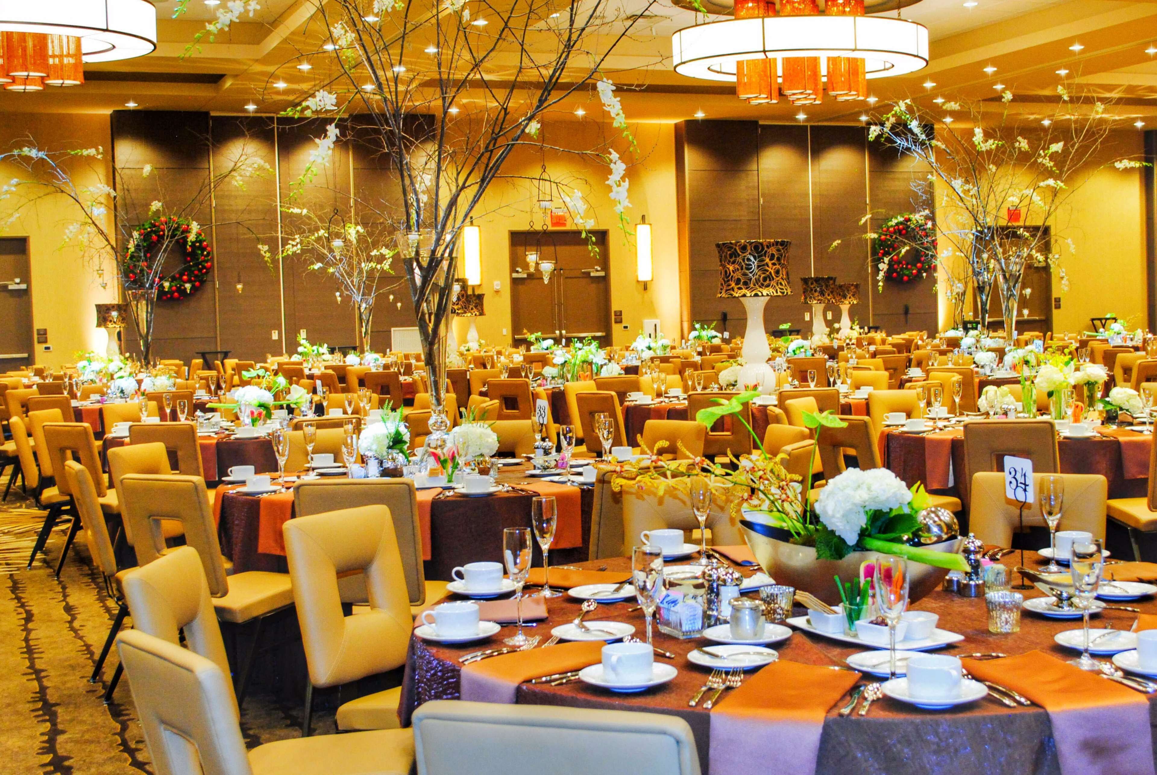 Un salón de banquetes con mesas redondas dispuestas para cenar, con centros de mesa florales e iluminación cálida.