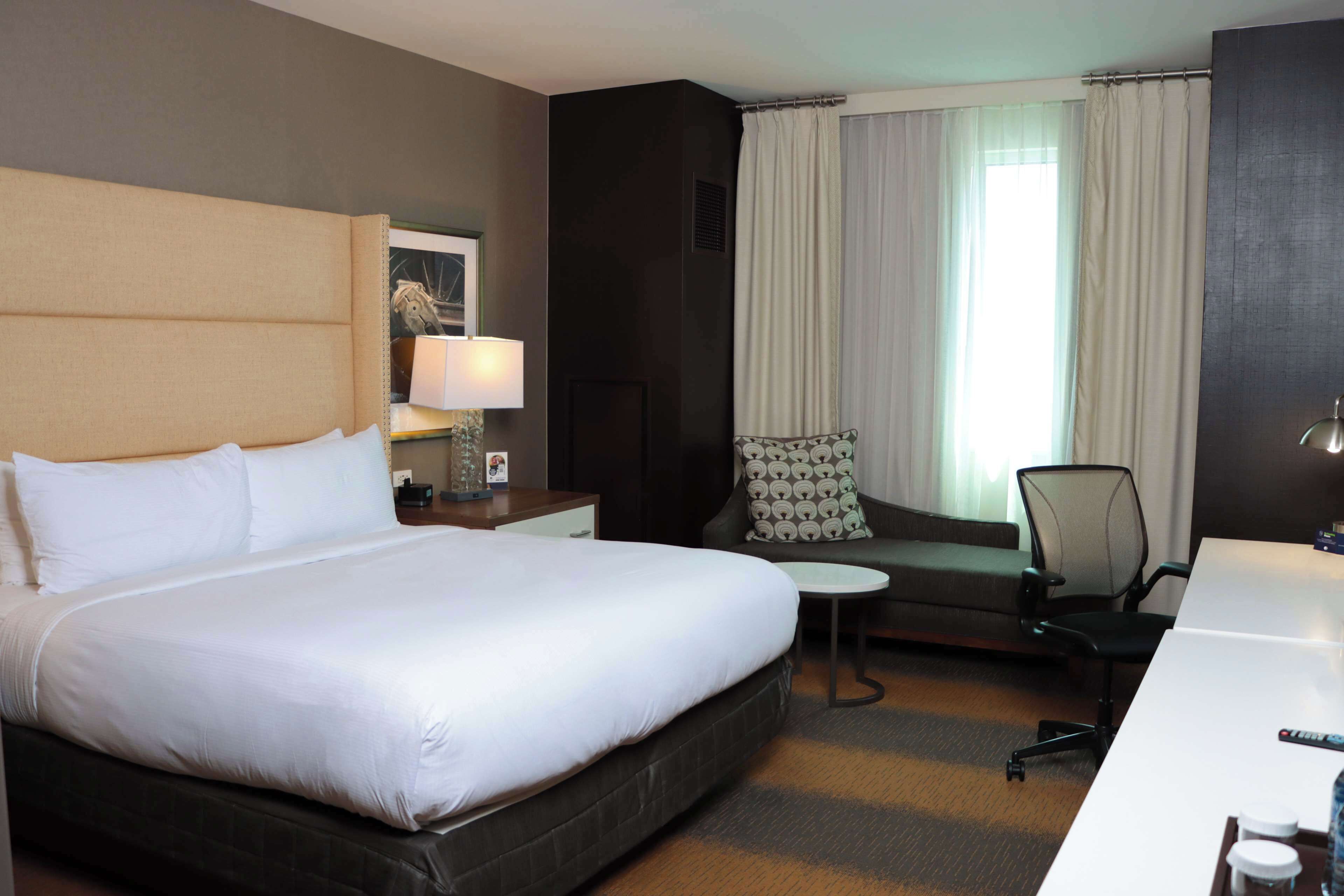 A hotel room with a large bed, a desk, a chair, a small table, and a window with curtains.
